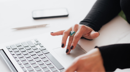Hand mit schwarzem Nagellack und türkisfarbenem Ring bedient Laptop-Touchpad, symbolisiert Downloadbereich